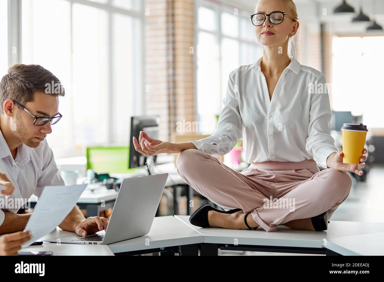 Gestresste Frau bei der Arbeit ruhig zu halten, Gleichgewicht der psychischen und psychischen Gesundheit zu halten, sitzt meditierend während Brainstorming, auf dem Tisch Stockfoto