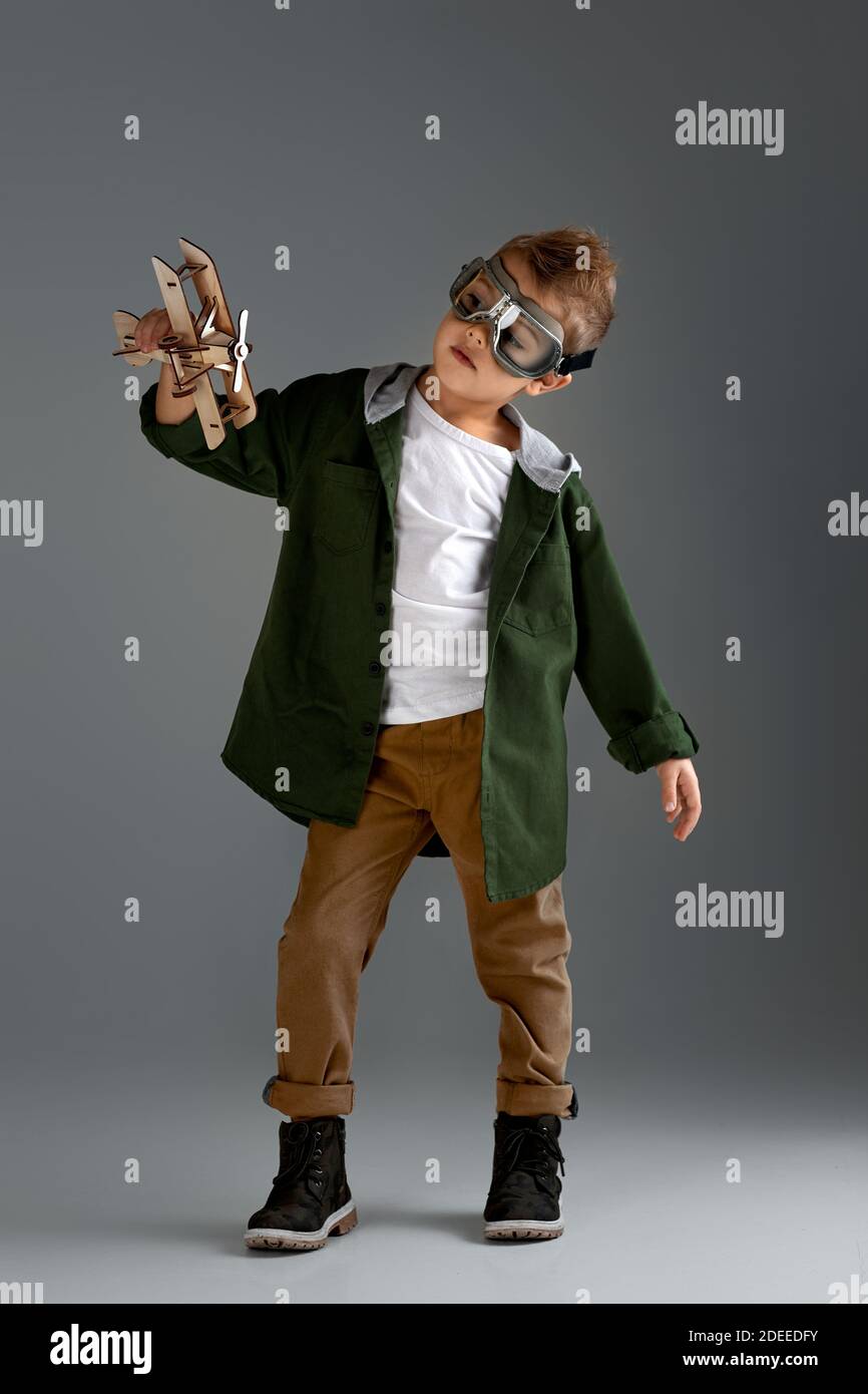 Happy Kind Junge in RetroBrille spielt mit Holzspielzeug Flugzeug auf StudioHintergrund. Traum