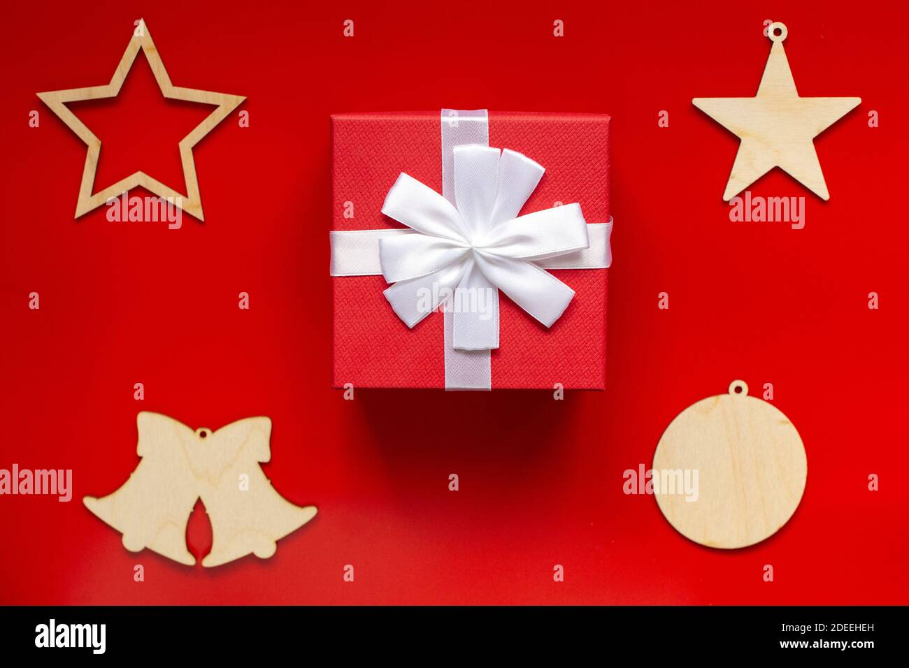 Rote Geschenkbox mit weißer Schleife und weihnachtlichen Holzdekorationen in Form von Sternen, Glocken und Ball, auf rotem Hintergrund Stockfoto