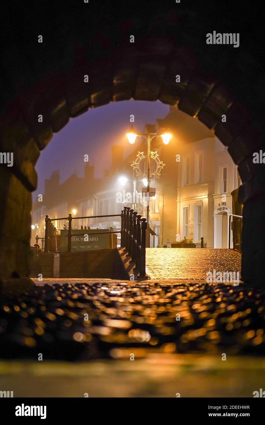 Blick durch den Tunnel bei Nacht mit Blick auf die stimmungsvolle britische Straßenszene; Straßenbeleuchtung beleuchtet die traditionellen Kopfsteinpflasterstraßen und Geländer am Fluss Stockfoto