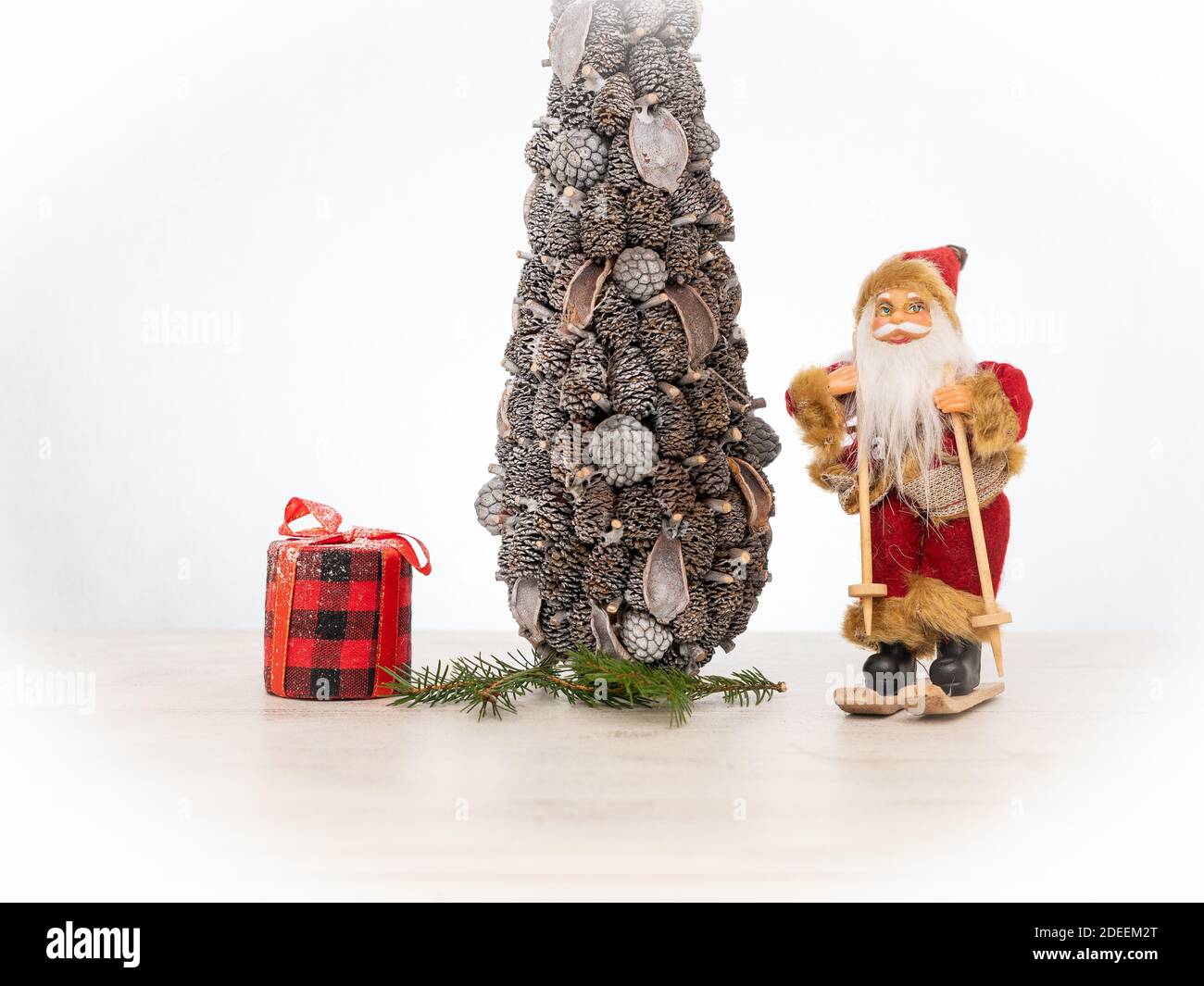 der weihnachtsmann auf Skiern steht neben einem weihnachtsbaum Und ein rotes Geschenk in einem Tartan kariert auf weiß Winterhintergrund Stockfoto