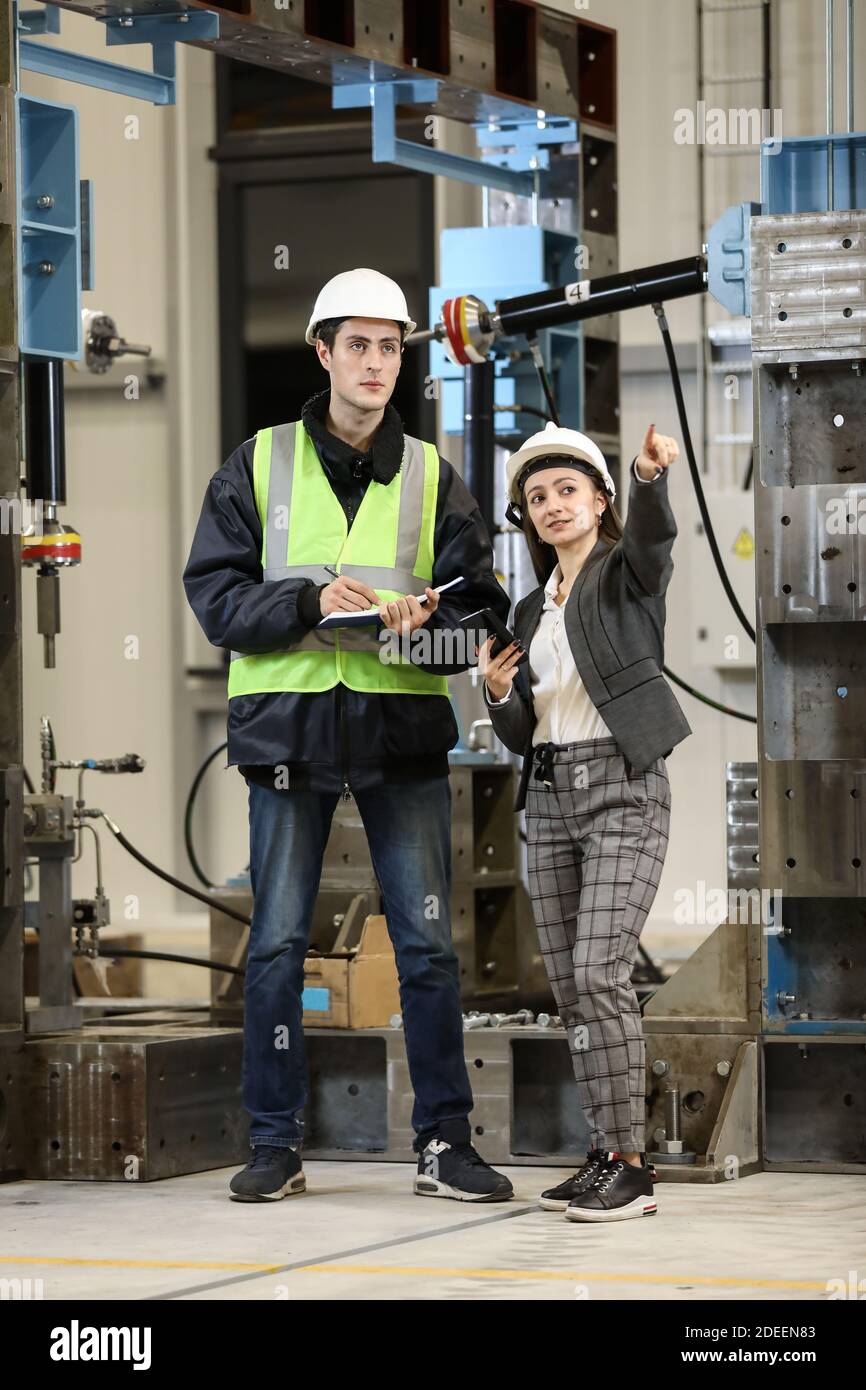Porträt einer weiblichen Betriebsleiterin in einem weißen Hut und Business-Anzug und Fabrikingenieurin in Arbeitskleidung. Steuerung des Arbeitsprozesses in der Fertigung. Stockfoto