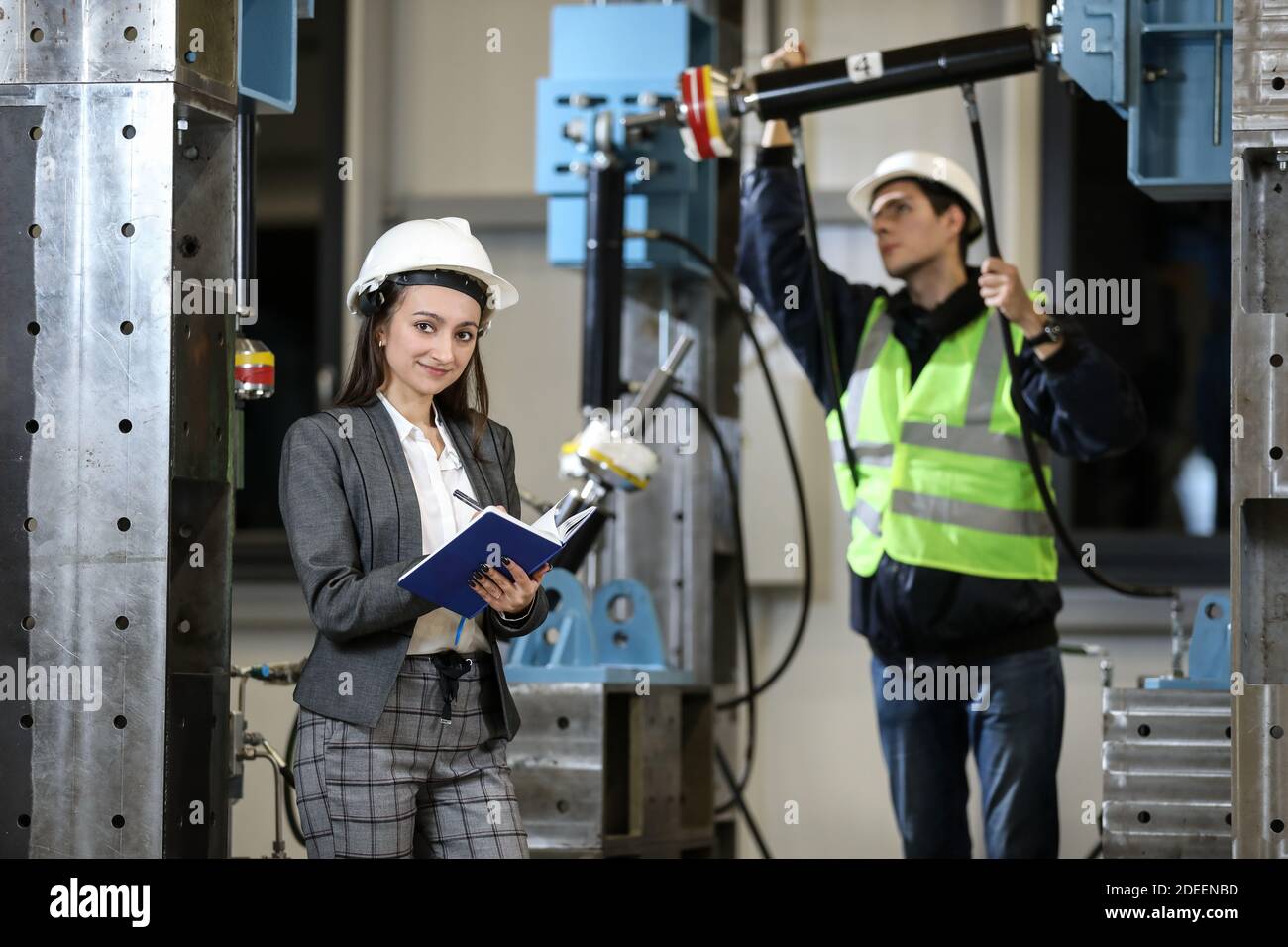 Porträt einer weiblichen Betriebsleiterin in einem weißen Hut und Business-Anzug und Fabrikingenieurin in Arbeitskleidung. Steuerung des Arbeitsprozesses in der Fertigung. Stockfoto