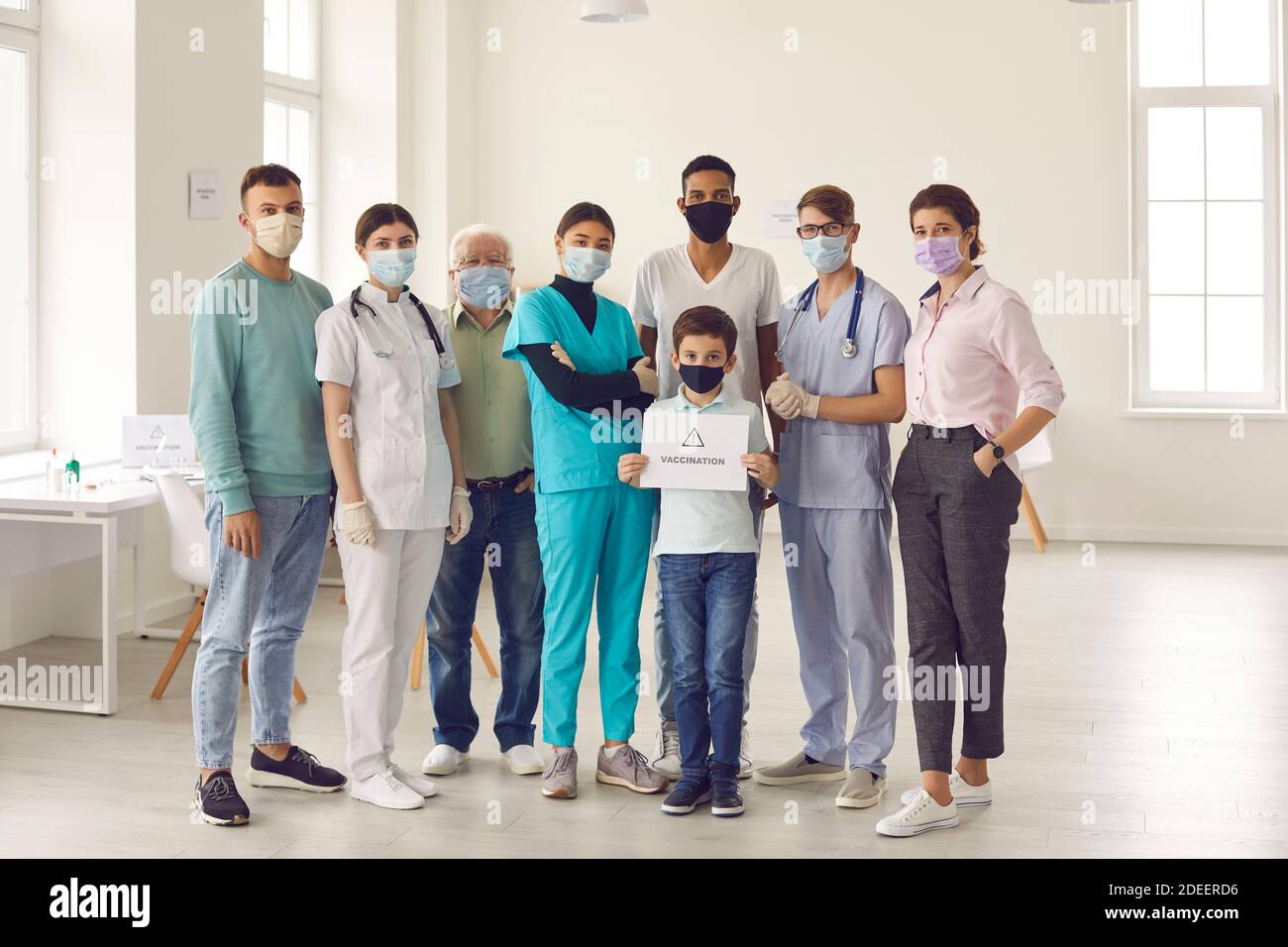 Gruppe von Erwachsenen mit kleinen Jungen, alle in Gesichtsmasken, ruft die Menschen für die Impfung Stockfoto