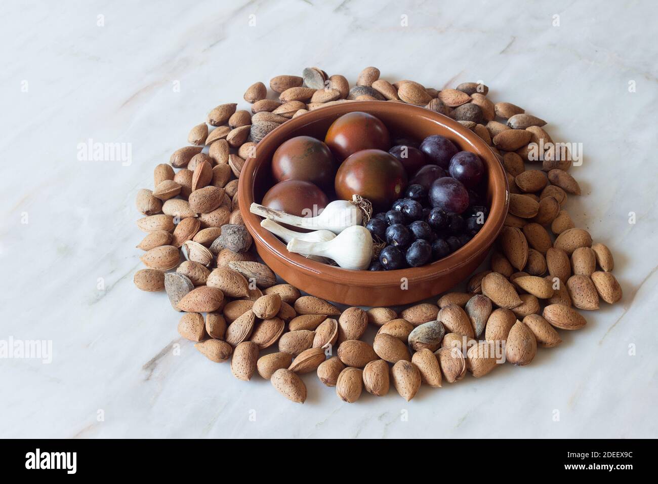 Eine Gruppe von Obst und Gemüse in einer runden Tonschale umgeben von Nüssen auf einem schönen rustikalen Marmortisch. Ökologische Produkte und gesunde Ernährung. Stockfoto