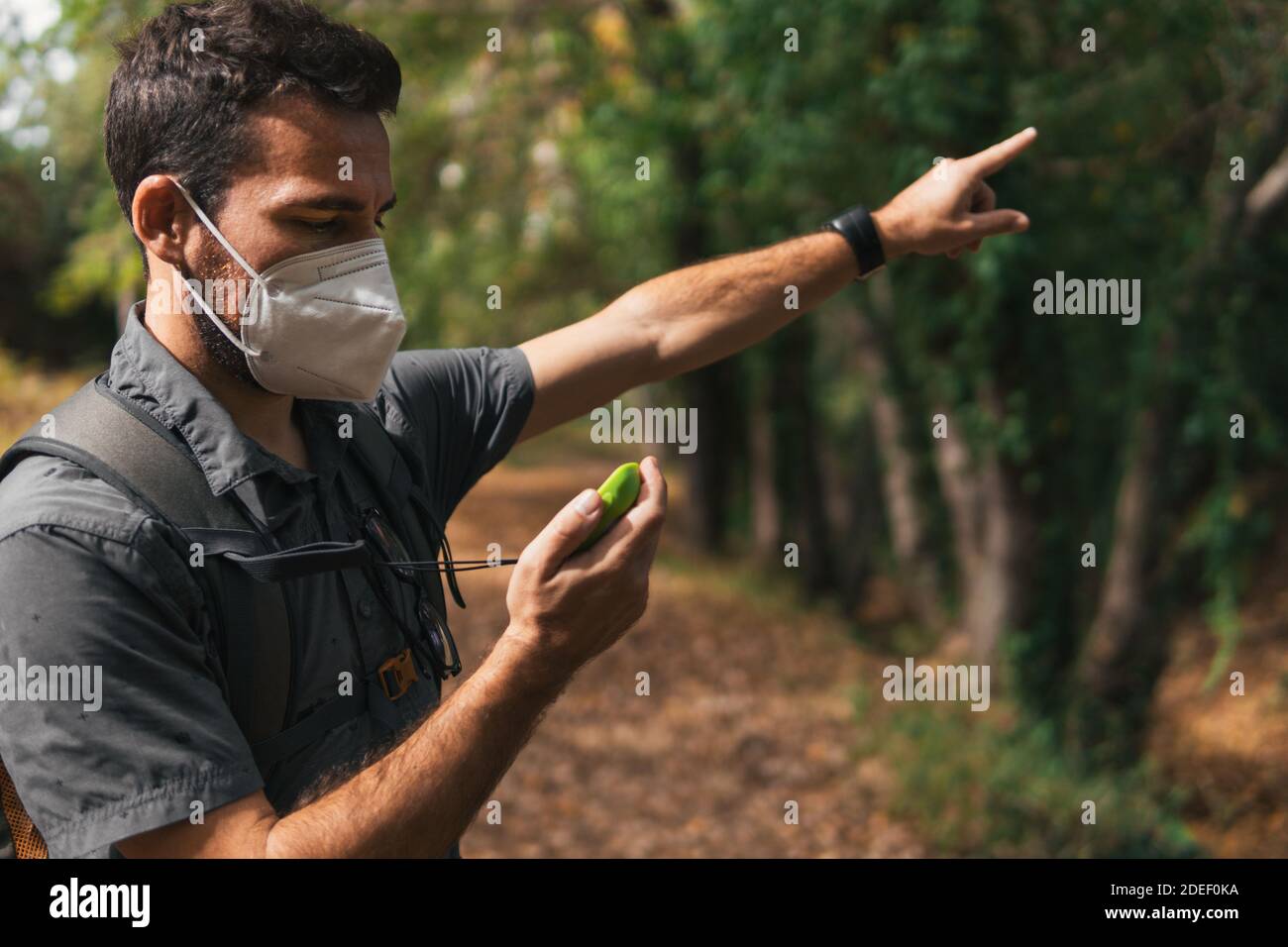 Mann, der auf das GPS schaut, der die Richtung der richtigen Route zeigt, während er im Berg mit einer Maske auf dem covid-19 wandert. Konzept des Sports. Stockfoto
