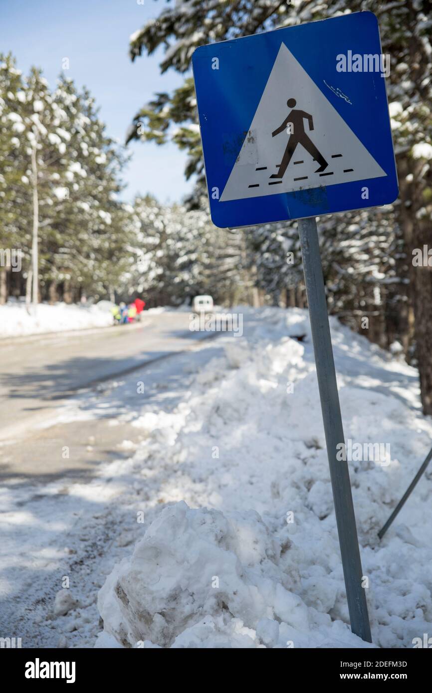 Ein Schild für eine Fußgängerüberfahrt auf einer Straße, die mit Schnee bedeckt und geräumt ist, so dass Autos passieren können. Stockfoto