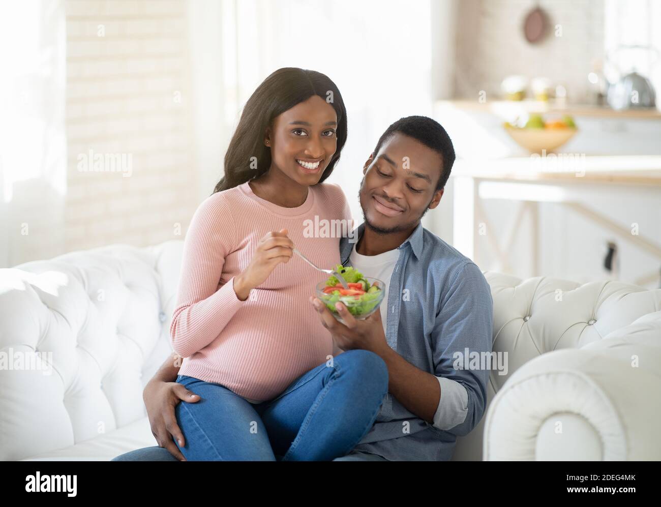 Gesunde Ernährung während der Schwangerschaft. Happy schwarz Freund und seine erwartungsvolle Freundin essen leckeren Gemüsesalat zu Hause Stockfoto