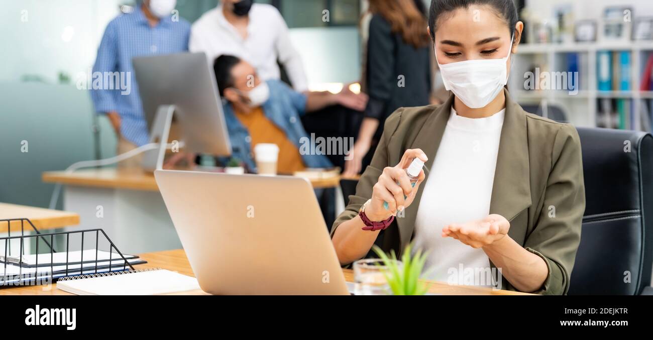 Panorama Asian Büro Mitarbeiter Geschäftsfrau tragen Gesichtsmaske verwenden Alkohol Sprühen Sie Handdesinfektionsmittel für die Hygiene im neuen normalen Büro mit Soziale Distanz PR Stockfoto