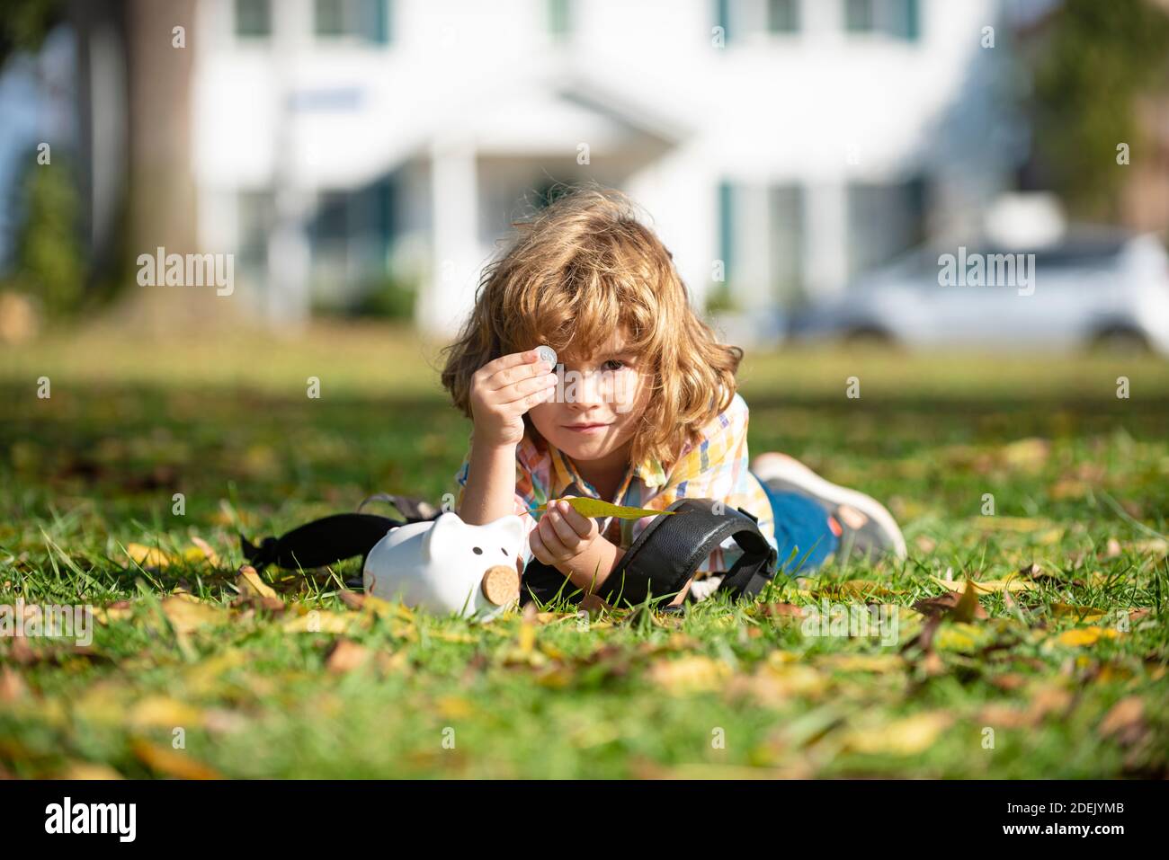 Outdoor-Porträt eines niedlichen kleinen Jungen hält Geld. Kinderersparnis mit einer Münze. Portrait Kind mit Sparschwein und Münze. Erste Schritte, um Geld zu sparen, Stockfoto