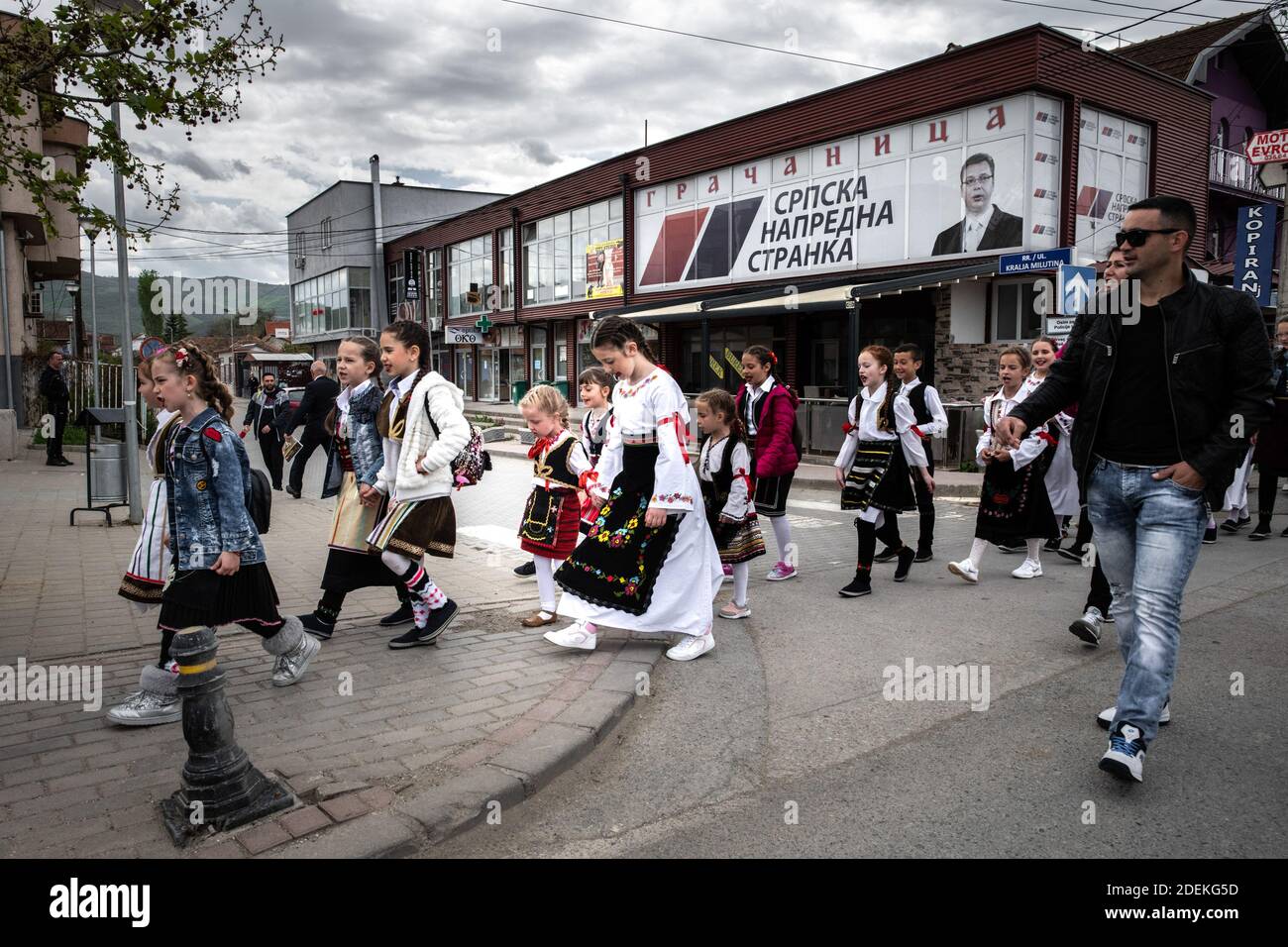 Gracanica, 29. April 2019. Le lundi apres paque, la communaute de gracanica, enclave serbe au sud de pristina, organisieren eine Zeremonie culturelle a la maison d ela culture de la ville. Les jeunes Teilnehmer porent les costumes traditionnels serbes. le cortège passe devant une affiche du Parti du Peuple Serbe. Stockfoto