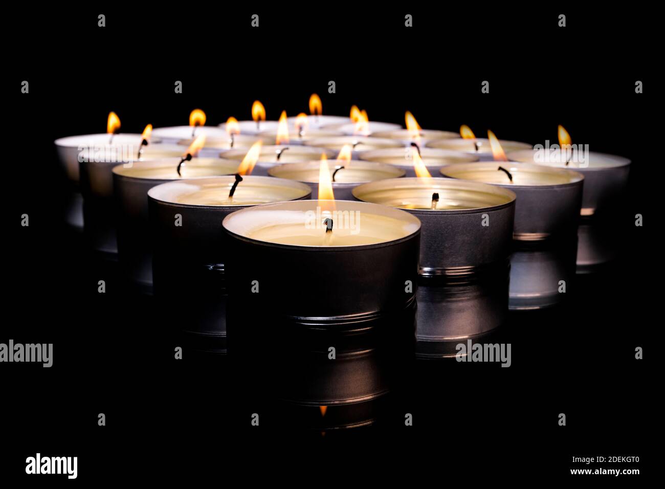 Selektiver Fokus und Nahaufnahme einer Anordnung von beleuchteten Teelichtkerzen auf dunklem Hintergrund. Entspannung und abstraktes Konzept. Stockfoto