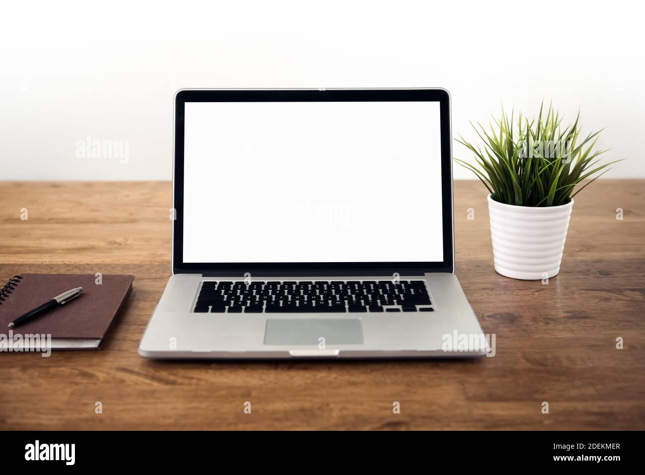 Leerer weißer Bildschirm Laptop-Computer mit Notebook-Stift und Zimmerpflanze auf Holztisch Stockfoto