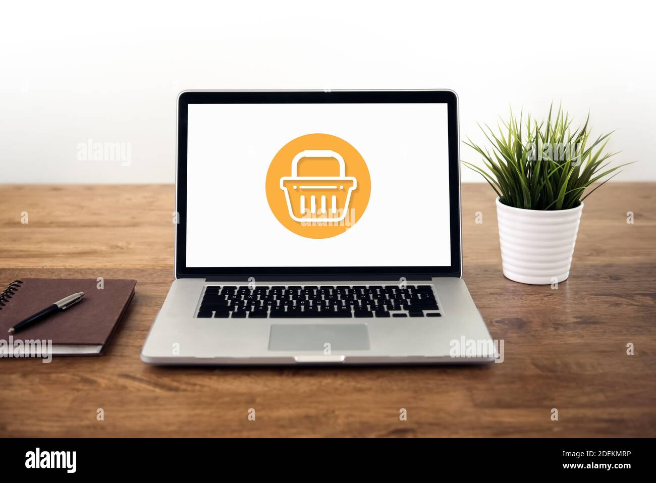 Laptop-Computer auf Holztisch mit Korbsymbol auf dem Bildschirm, Online-Home-Shopping und E-Commerce-Konzepte Stockfoto