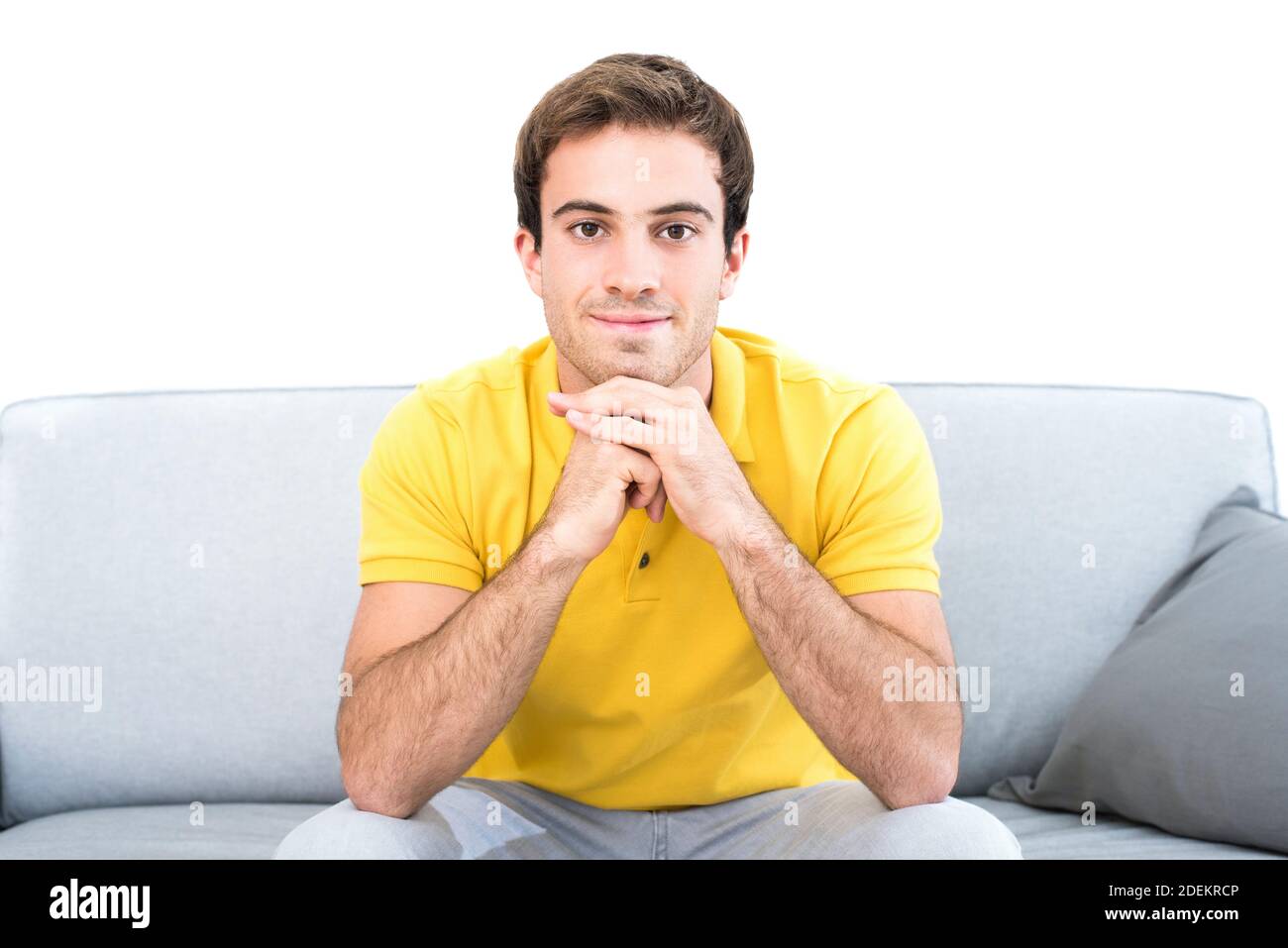 Junger gutaussehender lächelnder Kaukasischer Mann sitzt auf der Couch Wohnzimmer mit Blick auf die Kamera mit dem Kinn ruht auf Hände Stockfoto