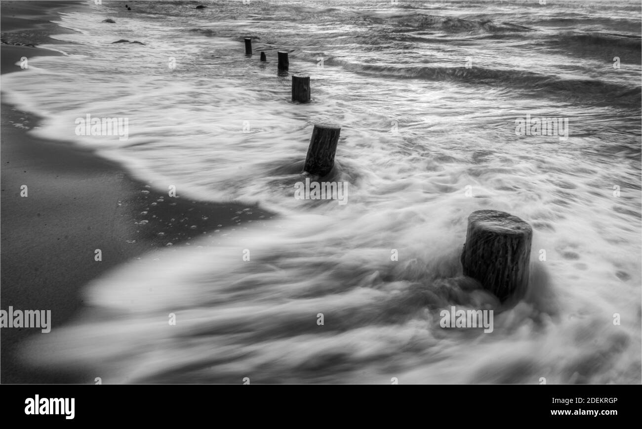 Wellen bewegen sich am Strand in schwarz und weiß Stockfoto