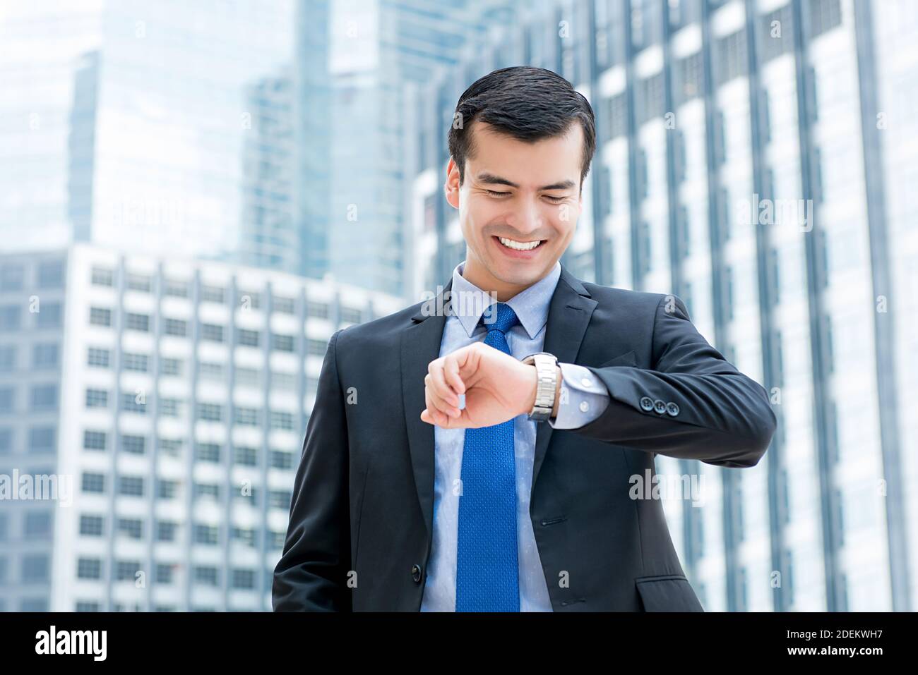 Geschäftsmann, der seine Armbanduhr anschaut, lächelt mit einem glücklichen Moment in der Stadt, während er auf einen Freund, Kollegen oder Termin wartet. Stockfoto