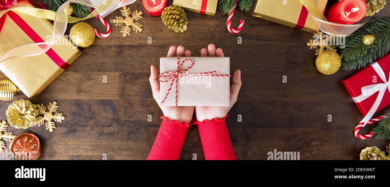 Frau in einem roten Pullover geben ein Geschenk auf einem Holztisch mit anderen Boxen und Dekorationsartikel umgeben, Vorbereitung für Weihnachtsfeier und Holid Stockfoto