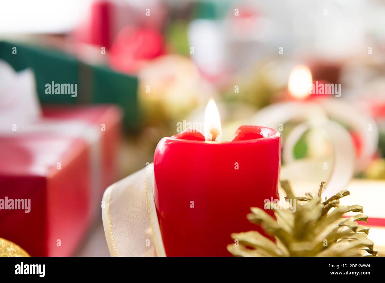 Brennende Weihnachtskerze auf dem Tisch mit bunten Geschenkschachteln und Dekorationselemente im Hintergrund, Vorbereitung für die Feier der festlichen Jahreszeit Stockfoto