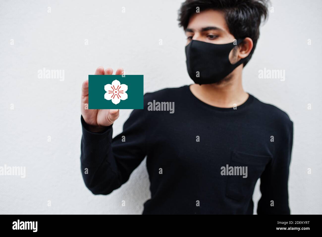 Japanischer Mann tragen ganz schwarz mit Gesichtsmaske halten Saga Flagge in der Hand isoliert auf weißem Hintergrund. Präfekturen von Japan сoronavirus Konzept. Stockfoto