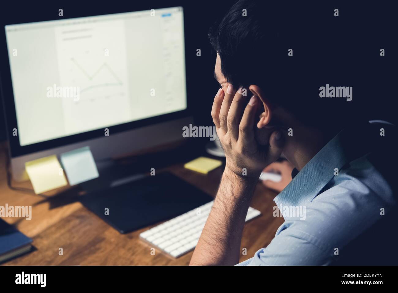 Müde und gelangweilter Mann, der nachts am Desktop-Computer arbeitet Überstunden machen, um sein Projekt zu beenden Stockfoto