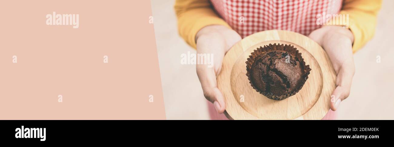 Eine Hausfrau gibt und präsentiert eine köstliche hausgemachte Schokolade Cupcake-Muffin, Panorama-Web-Banner mit Kopierraum Stockfoto