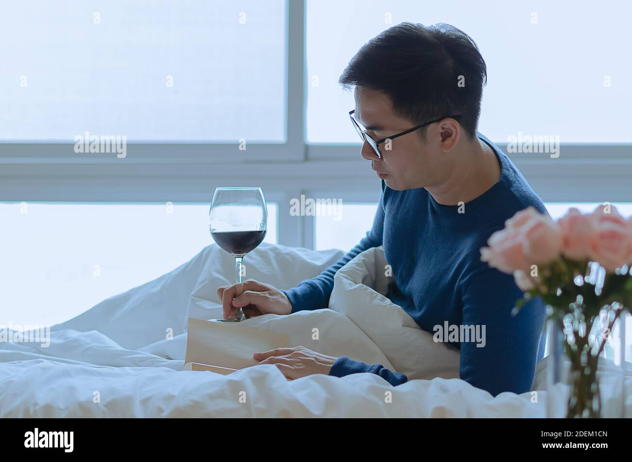 Eine Person liest Buch auf dem Bett mit einem Glas Rotwein. Digital Detox und Social Disconnect Konzept. Stockfoto