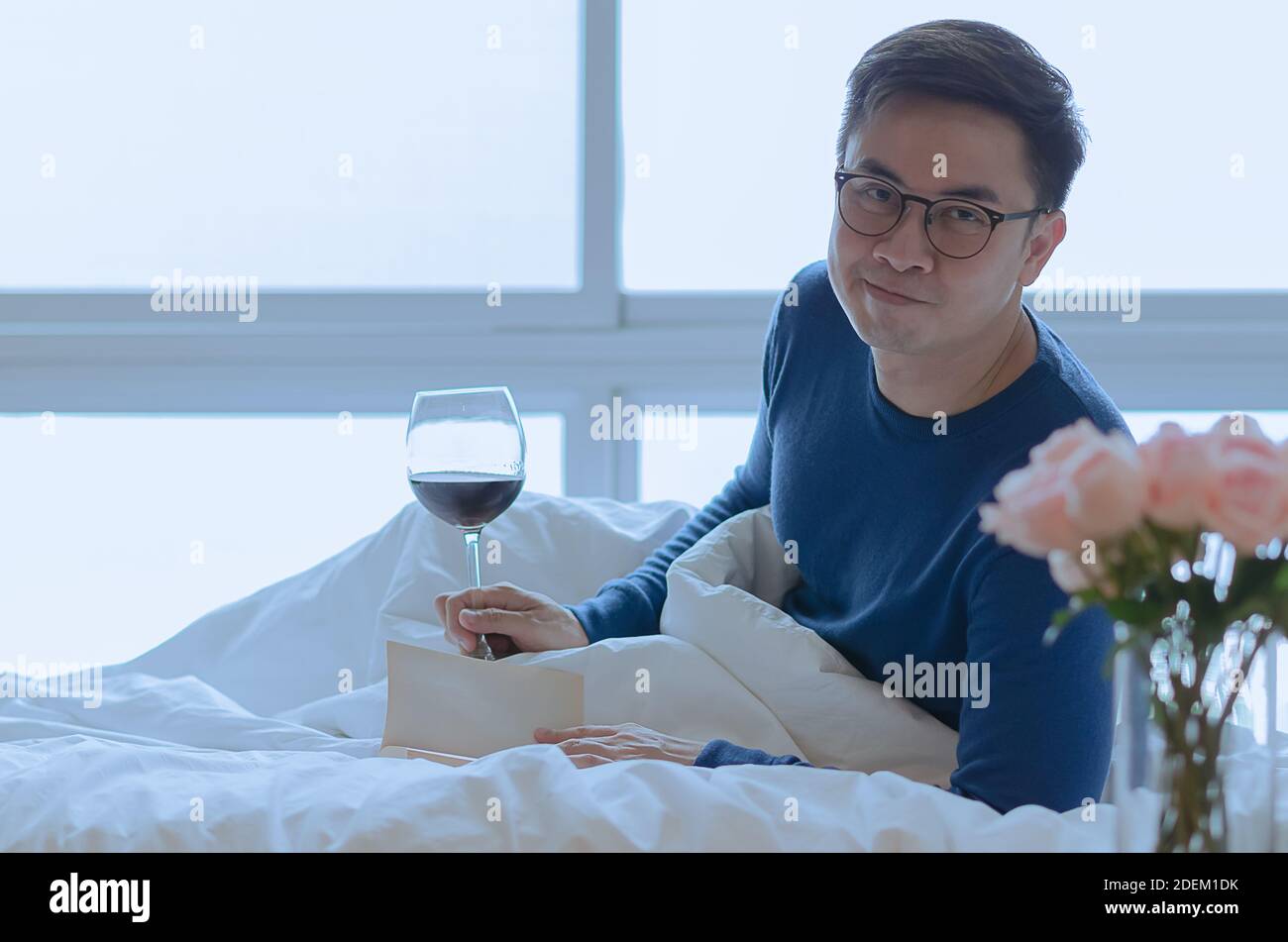 Eine lächelnde Person, die Buch auf dem Bett mit einem Glas Rotwein liest. Gute psychische Gesundheit Konzept. Stockfoto