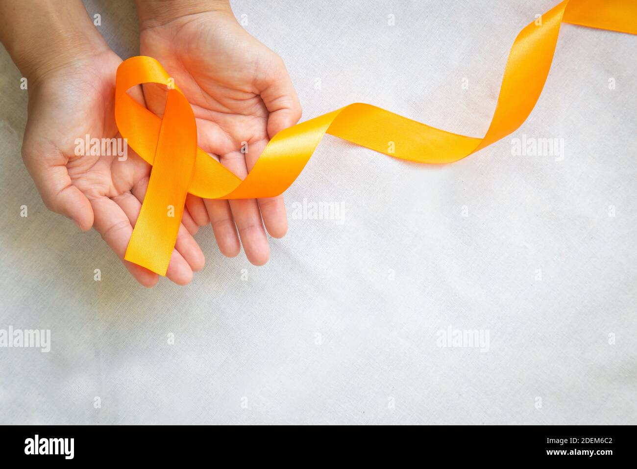 Hände mit orangefarbenem Farbband auf weißem Stoff mit Kopierfläche. Bewusstsein für Nierenkrebs, Leukämieerkrankungen, Bewusstsein für Hautkrebs, Weltkrebstag. Stockfoto