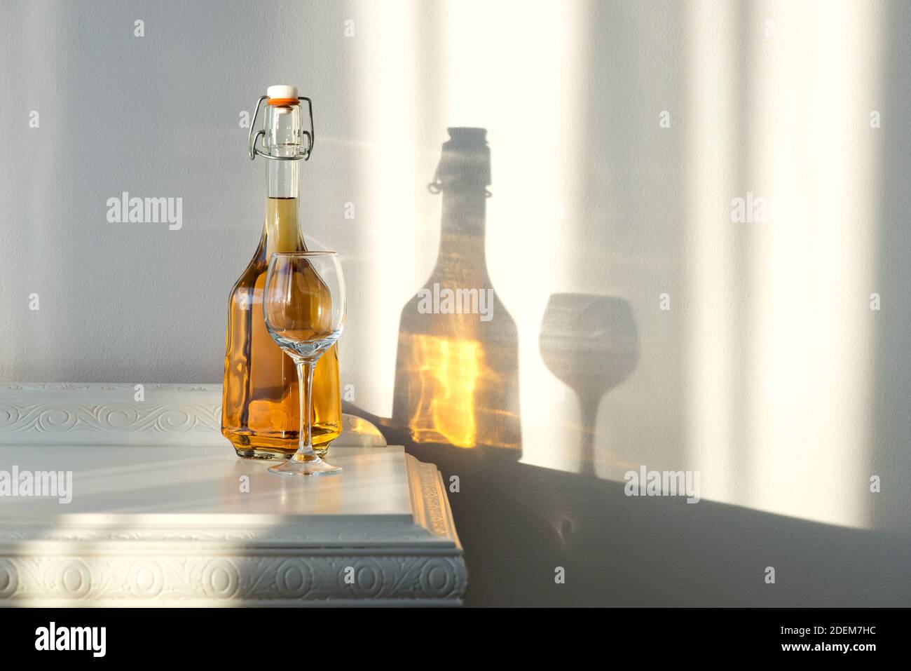 Elegante Flasche mit Alkohol und leerem Glas über einem Jahrgang Schrank und eine schöne Sonnenreflexion an der Wand - Kunstkonzept Stockfoto