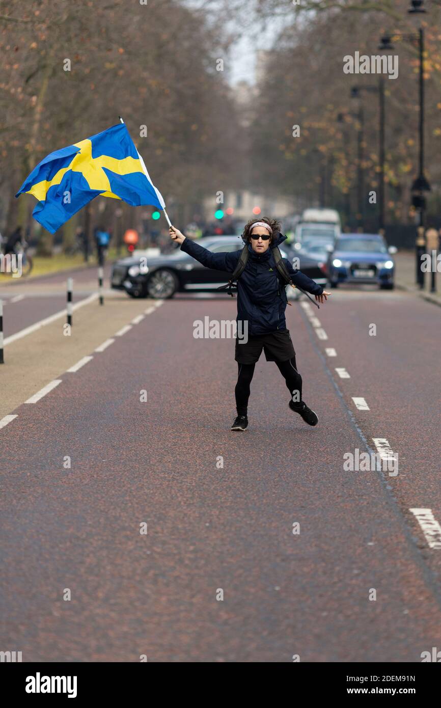 Anti-Lockdown Protest, Saint James's Park, London, 28. November 2020. Ein Protestler winkt mitten auf einer Straße mit der schwedischen Flagge. Stockfoto