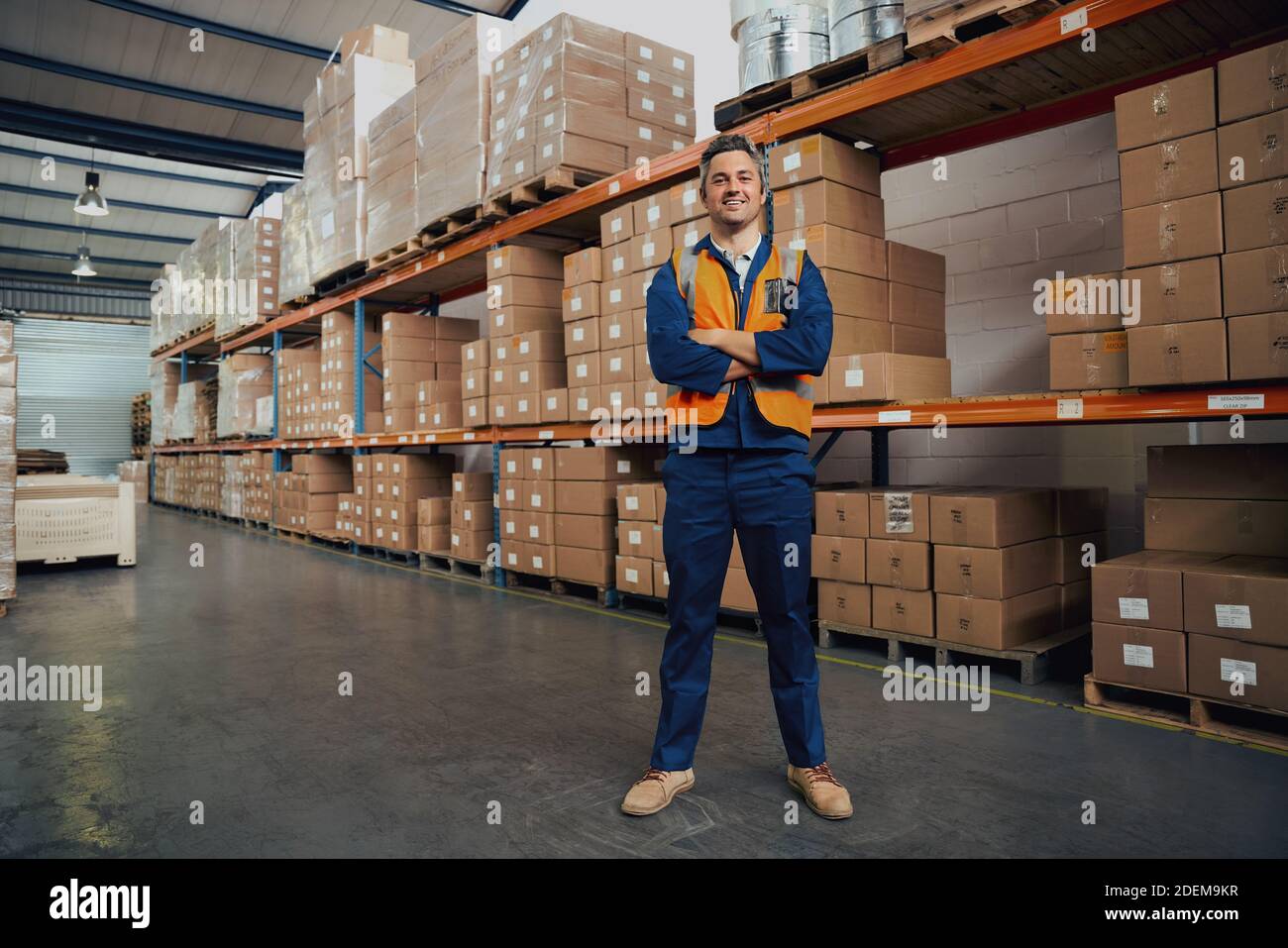 In voller Länge Ansicht eines Mannes mit gefalteten Händen stehend Im Werkslager Stockfoto