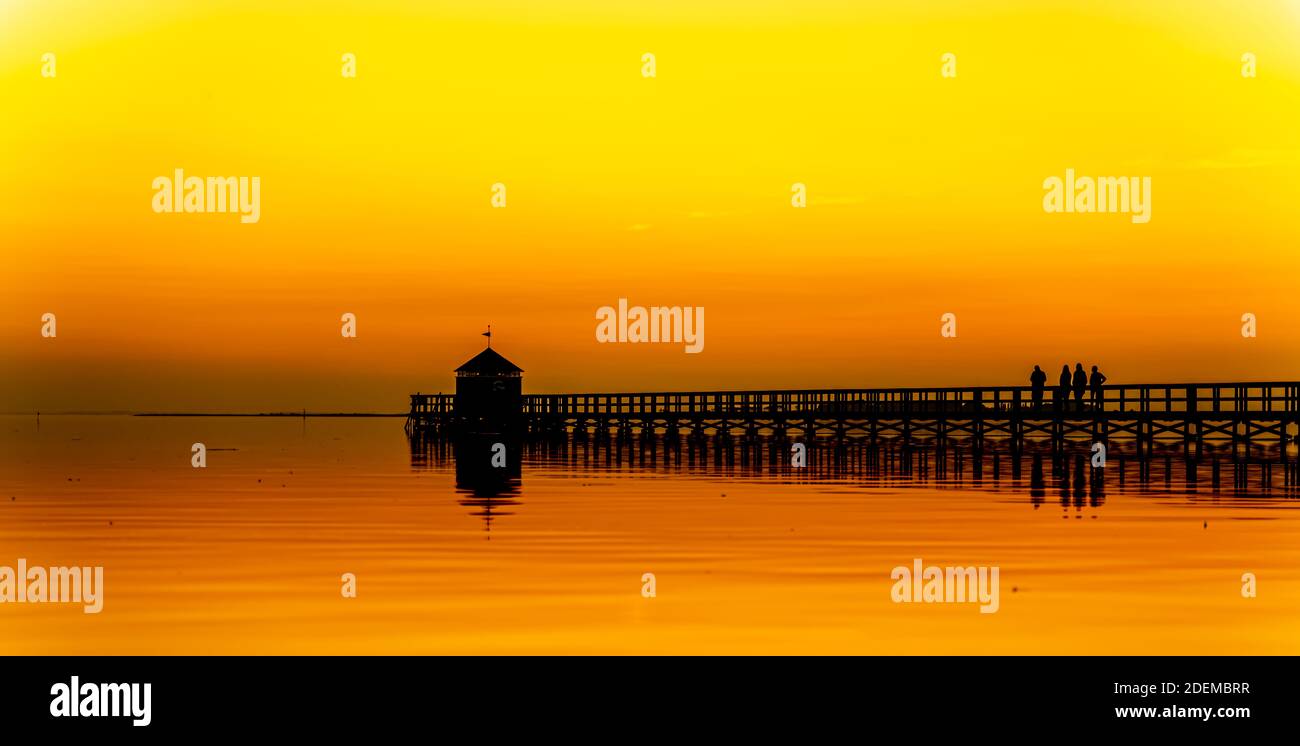 Großer hölzerner Pier an einem Strand kurz nach Sonnenuntergang, Brücke ist in schwarzer Silhouette und der Himmel von warmen Orangetönen vom Sonnenuntergang gesättigt. Stockfoto