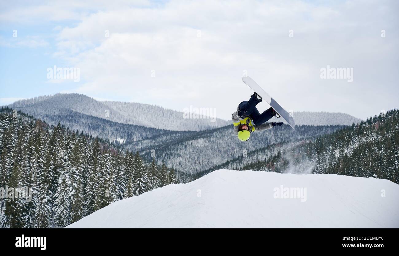 Horizontale Momentaufnahme von spektakulären Freeriding-Fliegen durch Snowboarder. Cooler Snowboardsprung am Hang gegen bewölkten Himmel und atemberaubende Berge im Hintergrund. Speicherplatz kopieren. Extremes Sportkonzept Stockfoto