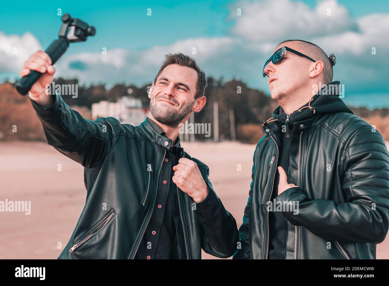 Zwei schöne männliche Freunde machen Selfie mit Action-Kamera mit Gimbal Stabilisator am Strand. Jugendliche Männer in schwarzen Kleidern Spaß haben, indem Sie Fotos Stockfoto