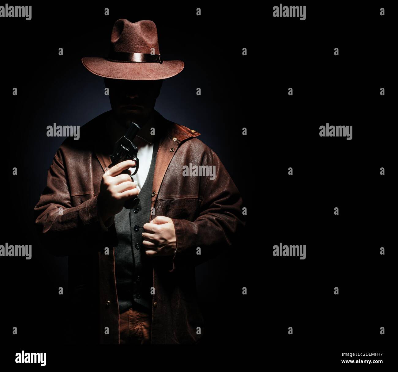 Foto eines schattigen Detektivs in Jacke und Hut mit einem Revolvergewehr auf schwarzem Hintergrund. Stockfoto