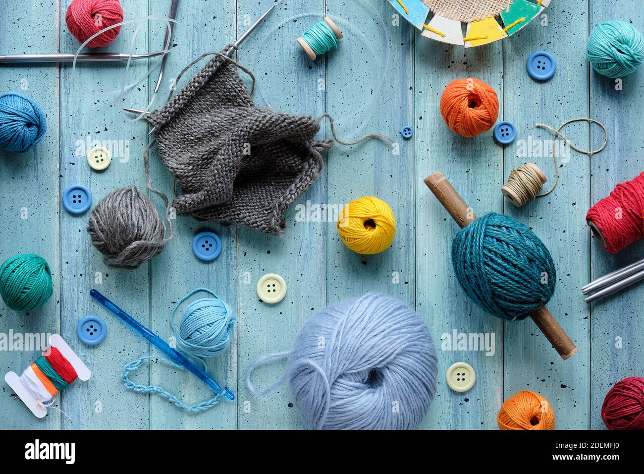 Wollbündel, Garnkugeln, Kordel. Häkel- und Stricknadeln auf hellem mintblauem Holz. Stockfoto