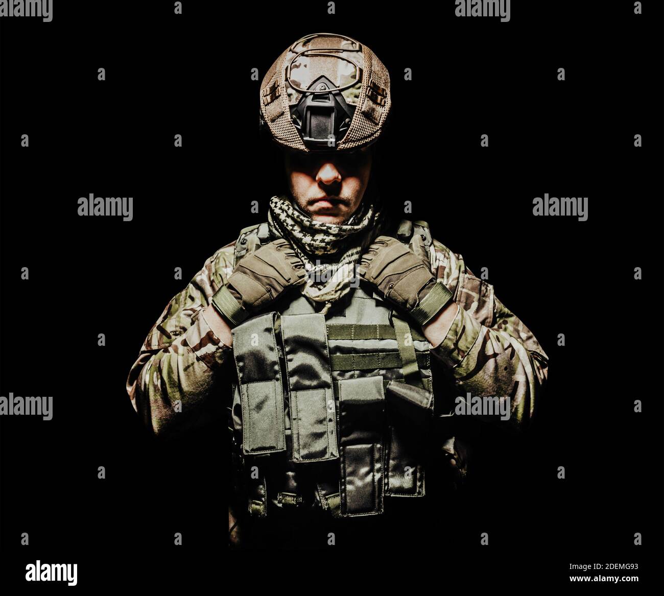 Foto eines voll ausgestatteten schattigen Soldaten in Panzerweste und Helm auf schwarzem Hintergrund stehen. Stockfoto