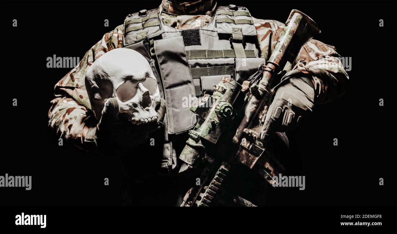 Foto eines voll ausgerüsteten Soldaten in Panzerweste mit automatischem Gewehr mit menschlichem Schädel. Stockfoto