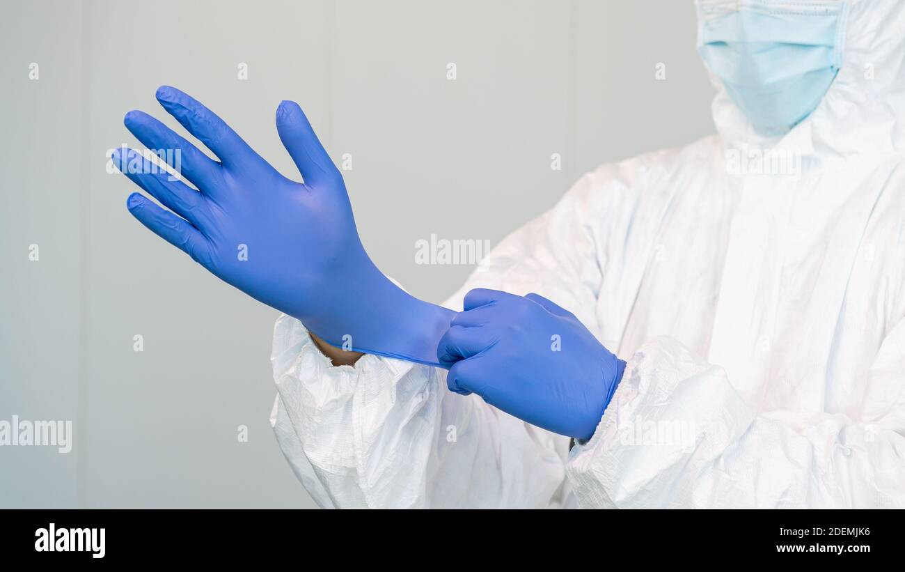 Ein Mitarbeiter des Gesundheitswesens bereitet sich darauf vor, indem er Handschuhe zur Behandlung von kovidierten Patienten aufsetzt. Die Krankenschwester trägt einen Schutzanzug PSA. Coronavirus Stockfoto