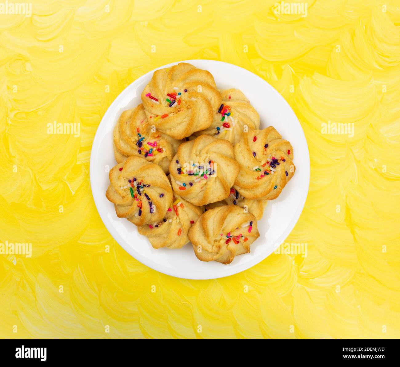 Draufsicht auf einen weißen Teller, gefüllt mit Shortbread-Keksen mit Streuseln auf einer gelb lackierten Tischplatte. Stockfoto