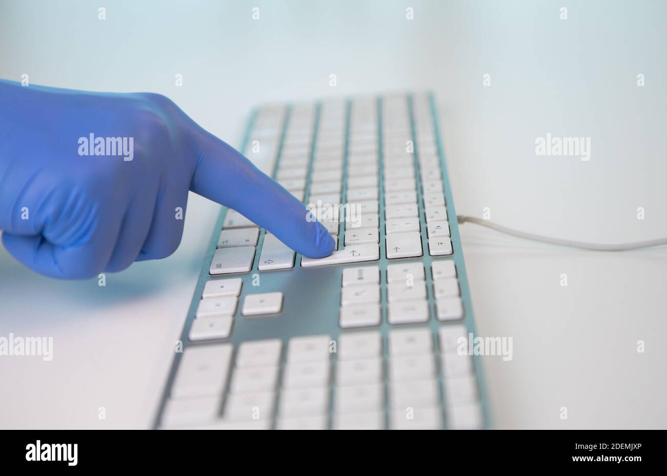 Handschuhen eines Arztes, der auf einer Computertastatur tippt. Drücken der ENTER-Taste. Konsultation eines Krankenhauses, wo Coronavirus oder Covid 19 ist Stockfoto