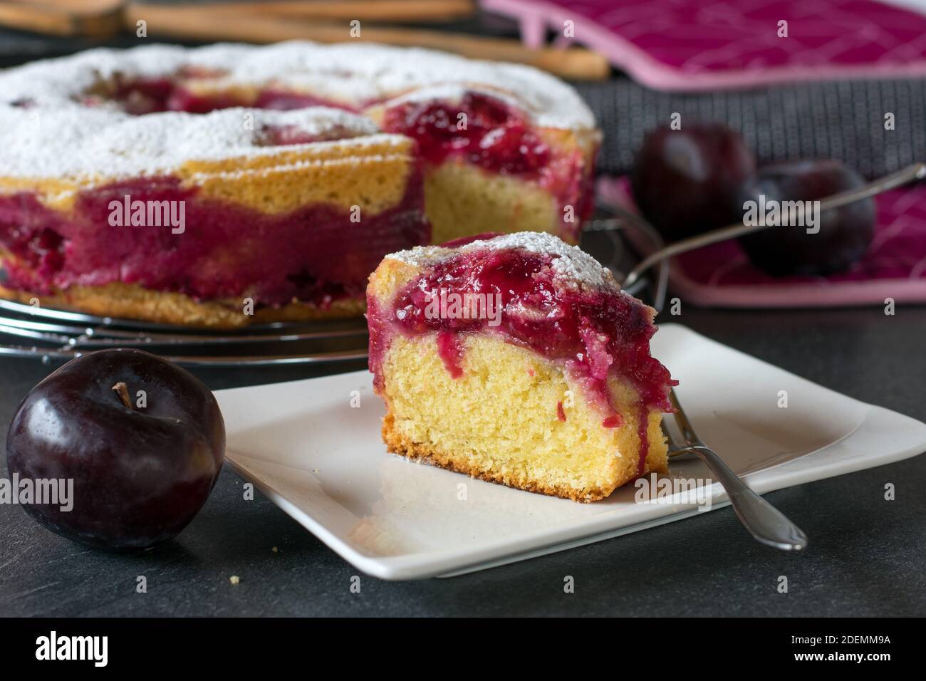 Ein Stück deutscher Pflaumenkuchen. Schwäbischer Pflaumenkuchen auf einem Teller. Der ganze Kuchen ist im Hintergrund zu sehen Stockfoto