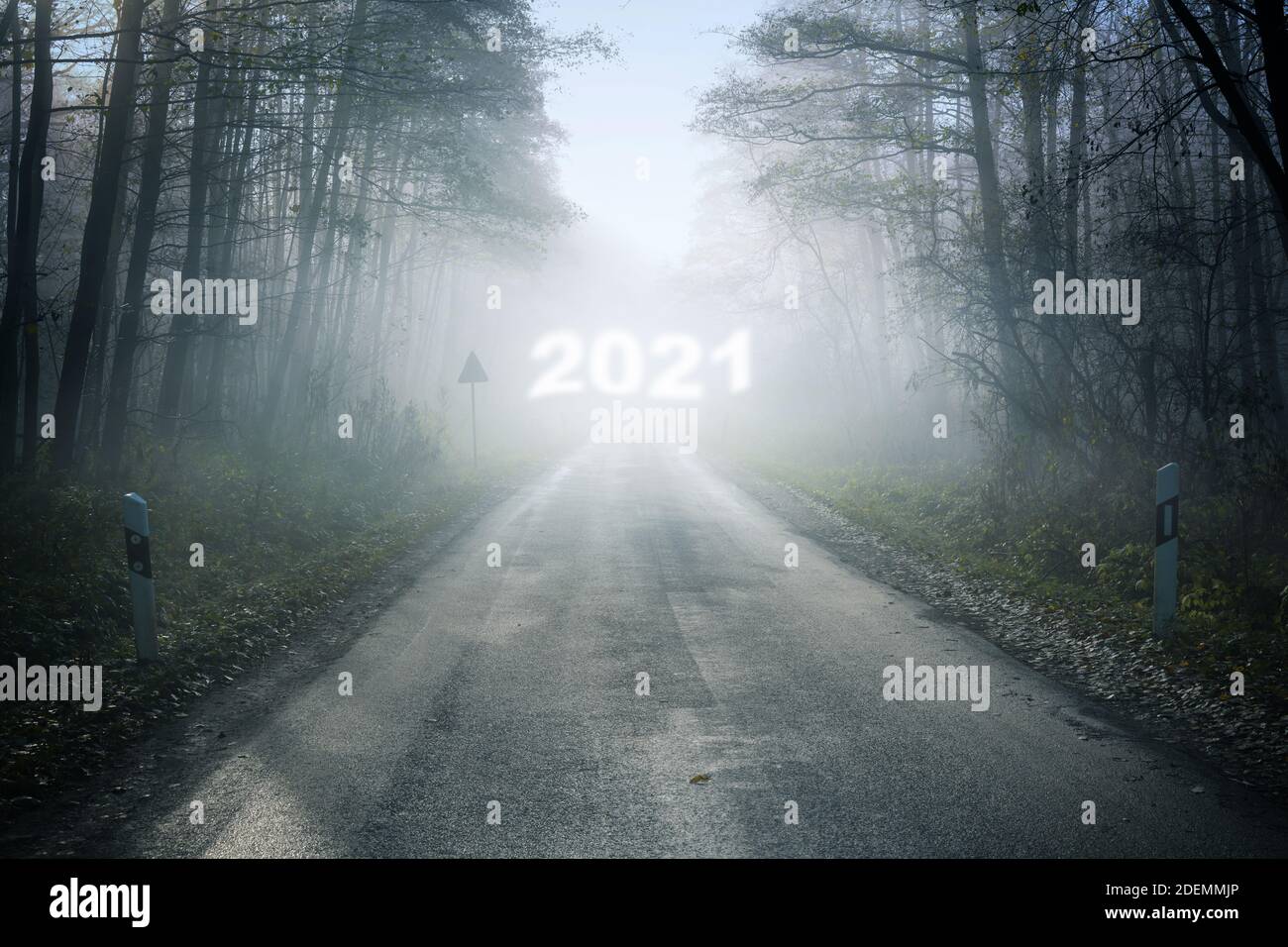 Neblige Landstraße mit verschwommener Neujahrsnummer 2021 im Nebel, die durch den Wald in eine ungewisse Zukunft führt, Urlaubskonzept, Kopierraum, se Stockfoto
