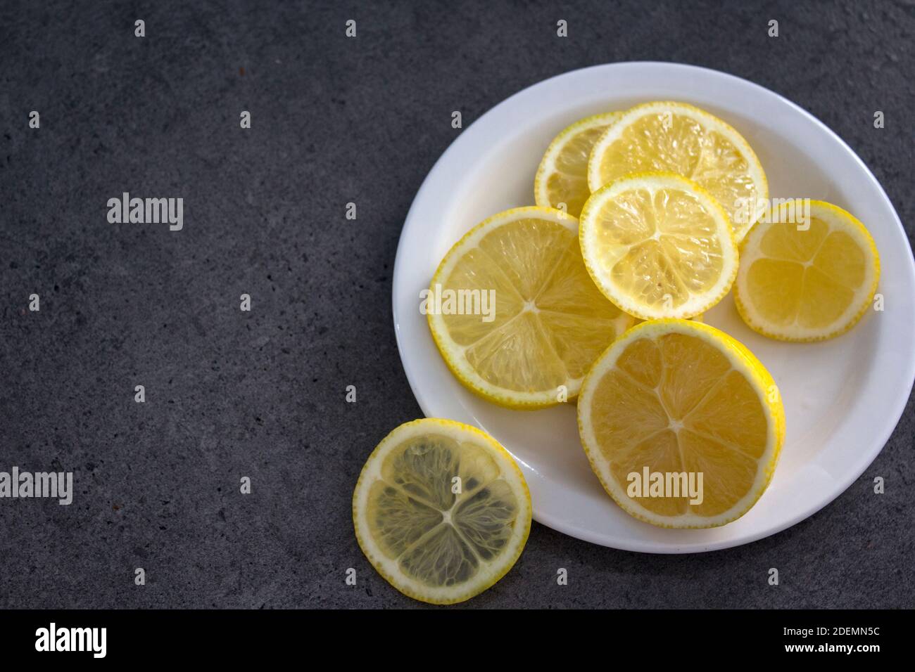 Zitronenscheiben auf weißem Teller. Grauer Hintergrund mit Kopierbereich. Stockfoto