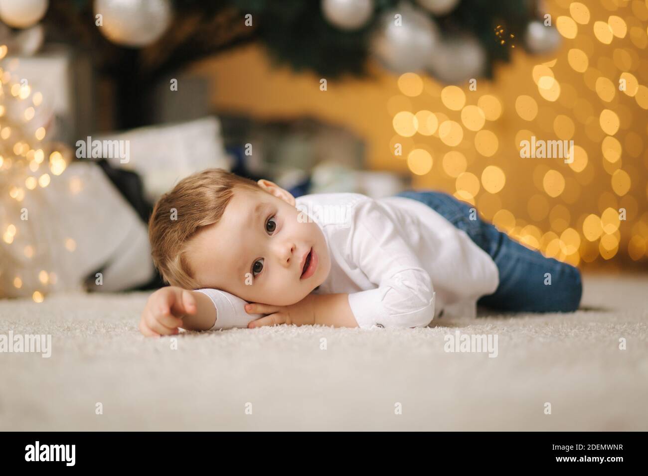 Niedlichen kleinen Jungen zu Hause durch den großen Weihnachtsbaum auf der Suche nach Geschenken. Happy Kid verbringen Sie Zeit im Urlaub und genießen jeden Moment Stockfoto