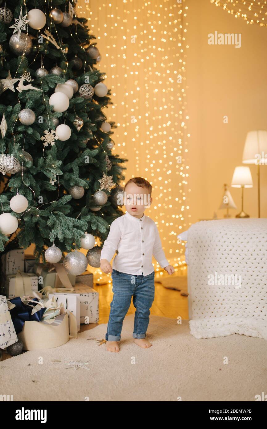 Niedlichen kleinen Jungen zu Hause durch den großen Weihnachtsbaum auf der Suche nach Geschenken. Happy Kid verbringen Sie Zeit im Urlaub und genießen jeden Moment Stockfoto