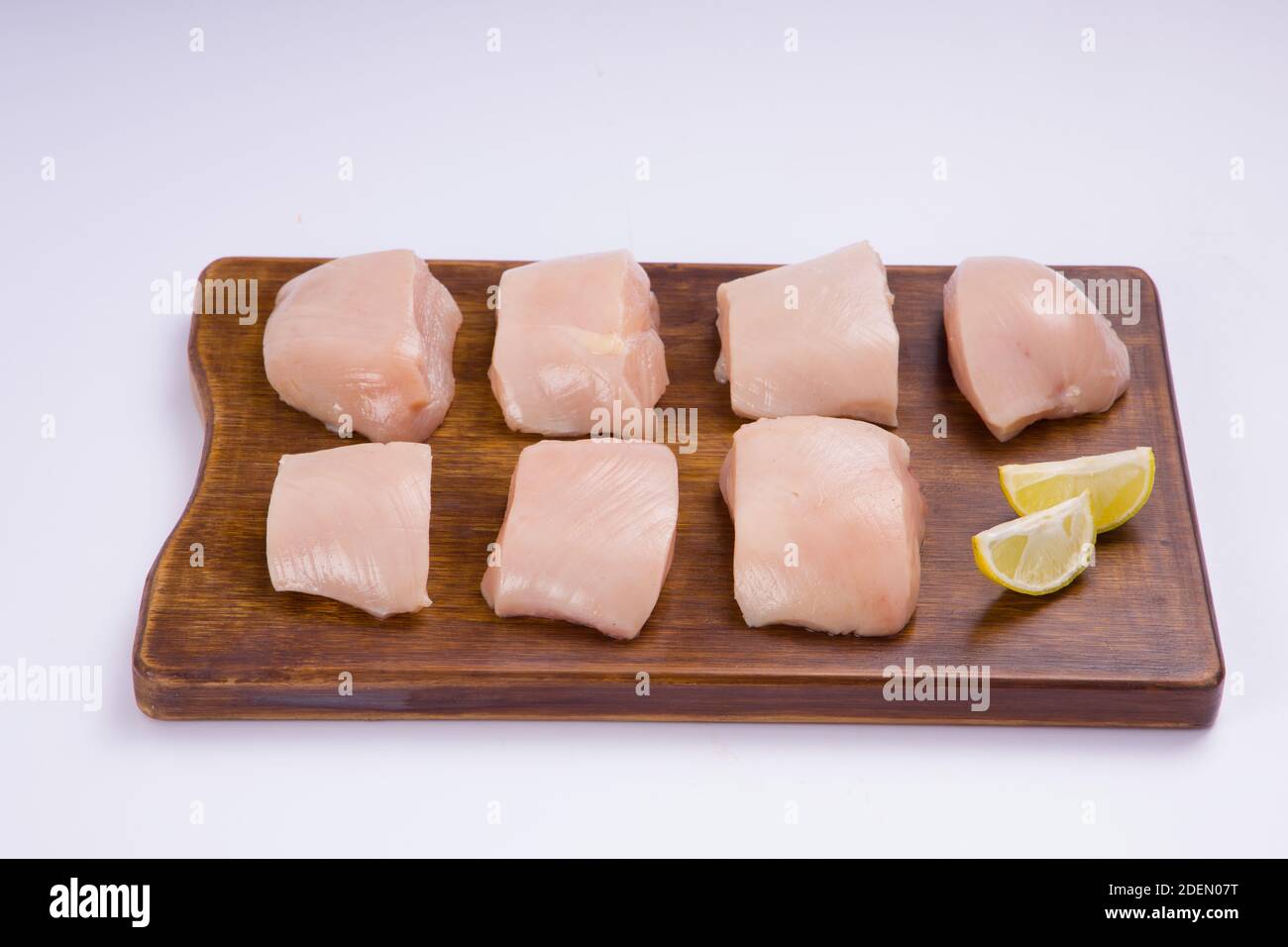 Rohes Huhn zart braten geschnitten ohne Haut auf Holz angeordnet Tafel und mit Zitronenscheiben auf weißem Hintergrund garniert Stockfoto