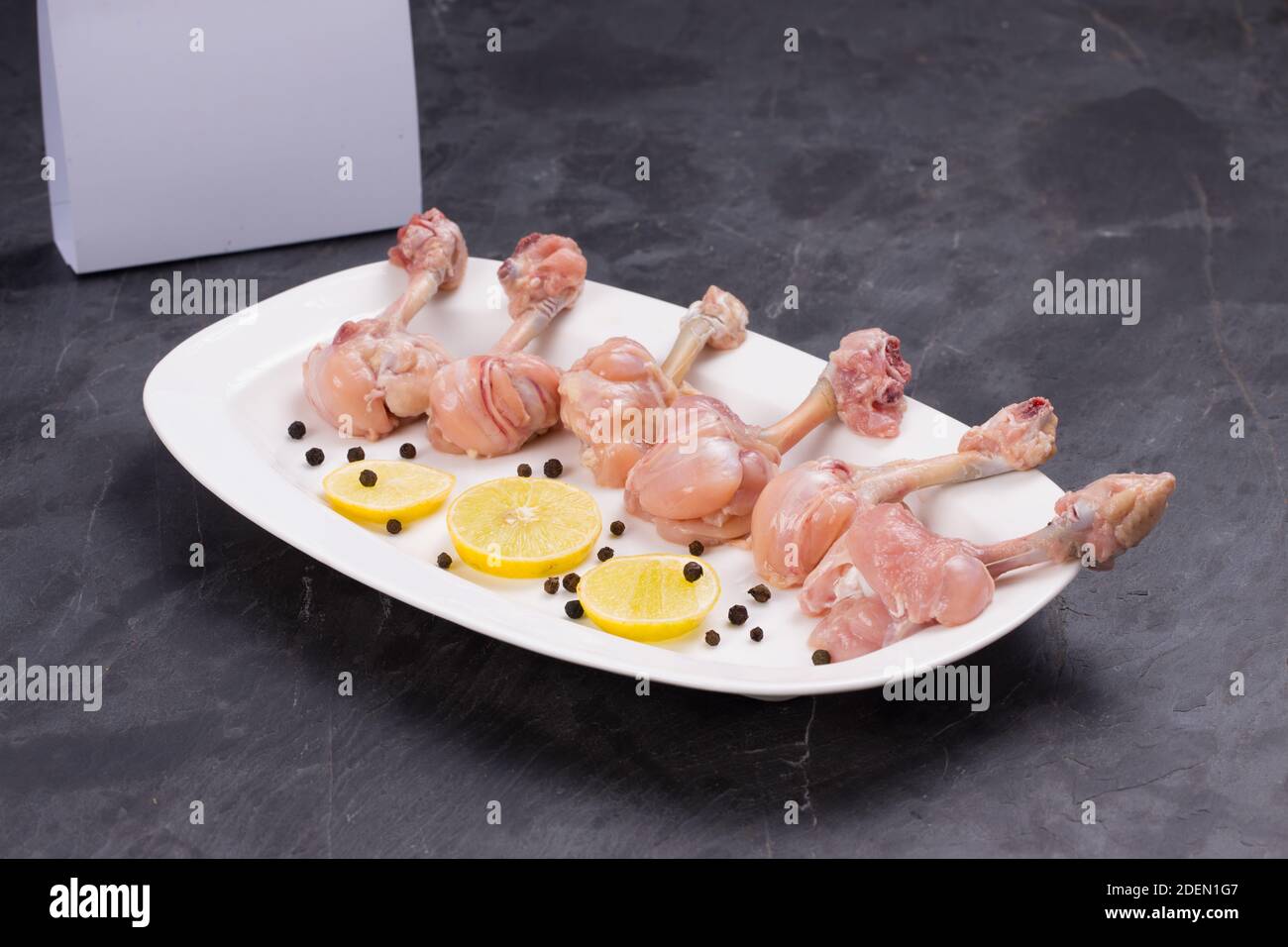 Rohes Huhn Lollipop, sechs Stücke Huhn Lollipop auf einem angeordnet Servierteller weiß und mit Zitronenscheiben und schwarz garniert Mit Lieferung pfeffern Stockfoto