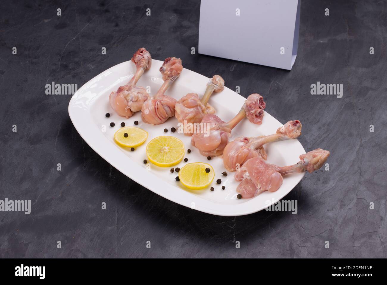 Rohes Huhn Lollipop, sechs Stücke Huhn Lollipop auf einem angeordnet Servierteller weiß und mit Zitronenscheiben und schwarz garniert Mit Lieferung pfeffern Stockfoto